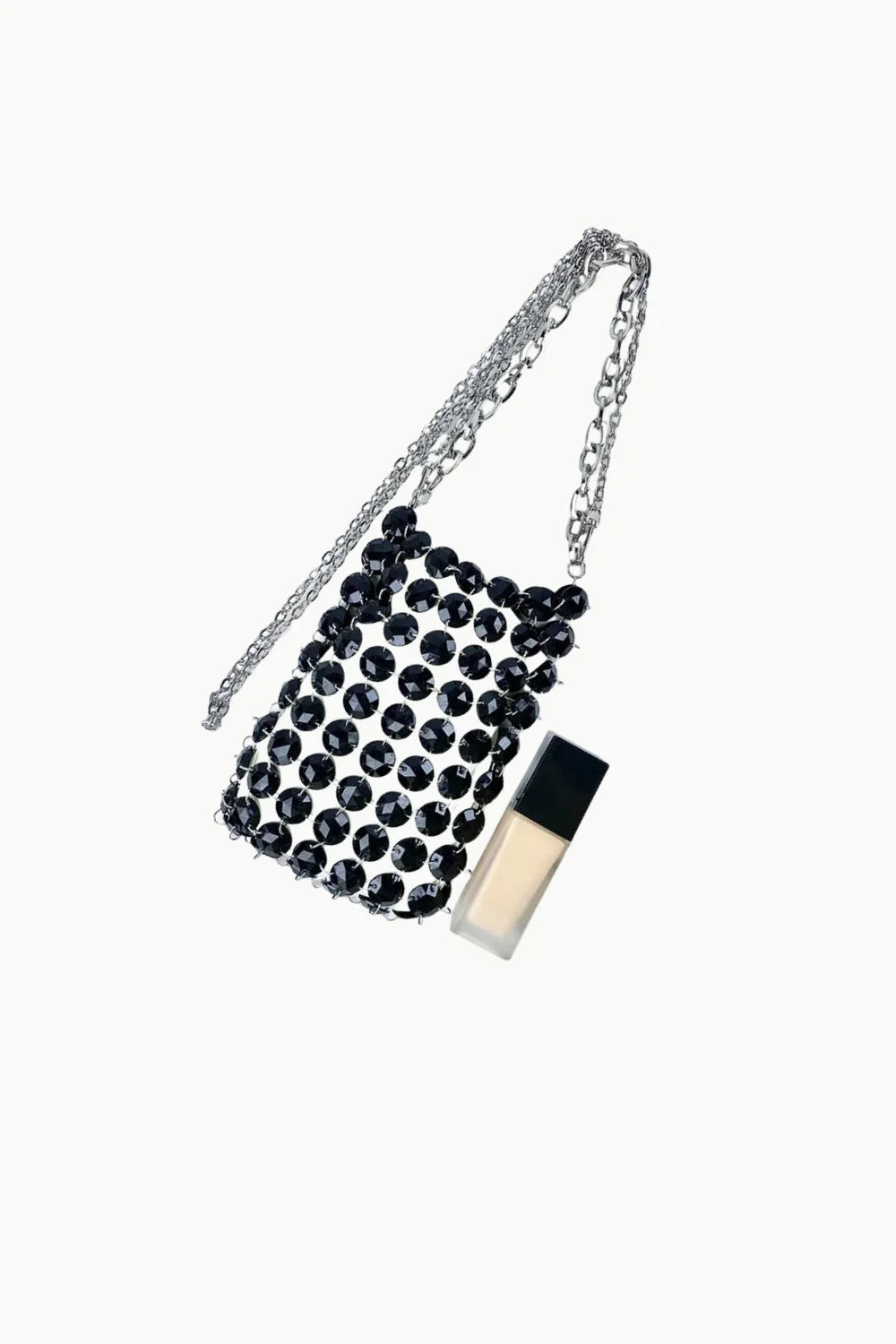 Black crystal beaded mini shoulder bag with silver chain strap next to liquid foundation