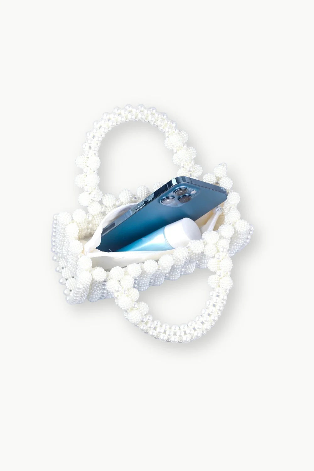 Women’s beaded bag with two handles holding a blue smartphone and white tube