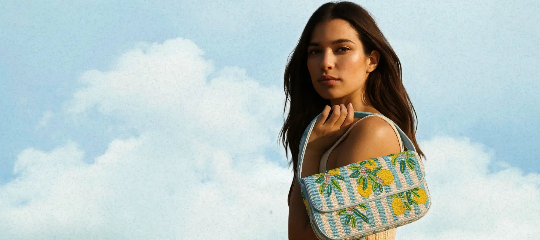 Model carrying a lemon-pattern beaded shoulder bag on shoulder against a sky backdrop