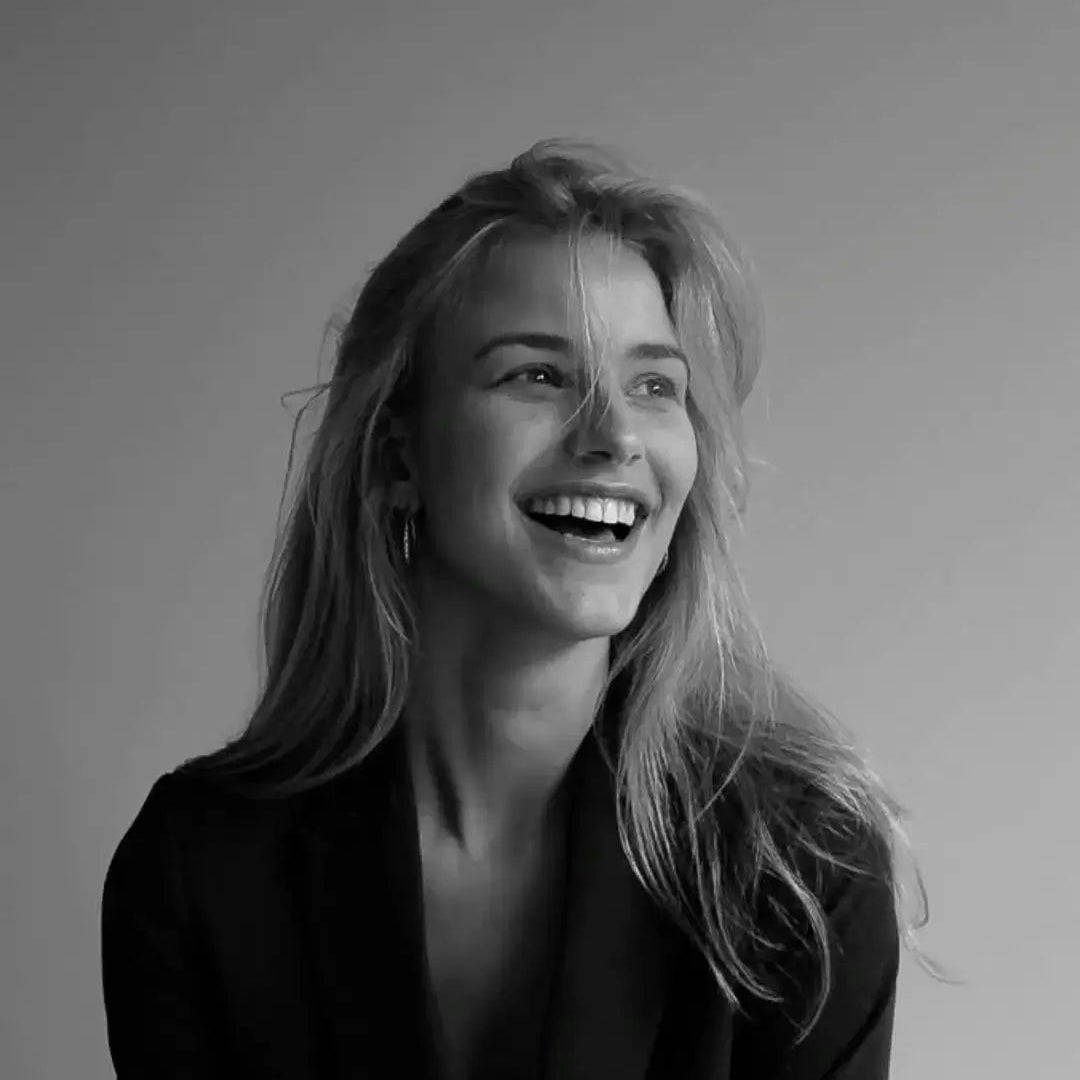 Smiling woman in black blazer, minimalist lifestyle portrait for Beaded Bag brand homepage.