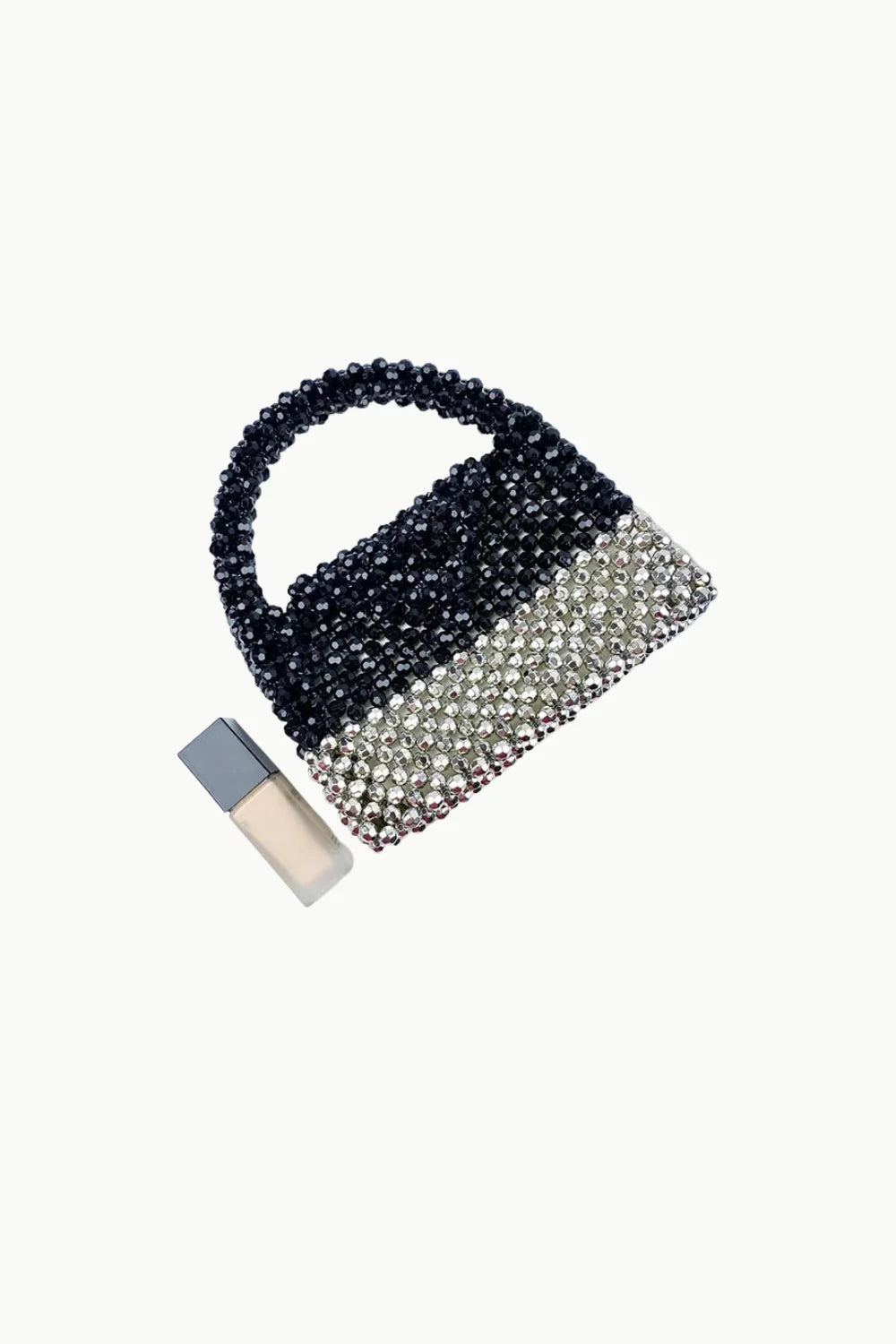 Black and silver beaded bag with top handle and a small bottle of liquid foundation