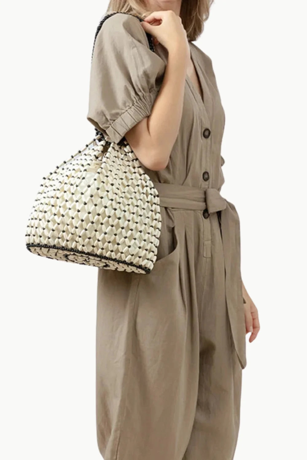 Woman in beige jumpsuit with black wooden beaded bag and woven straw bucket bag