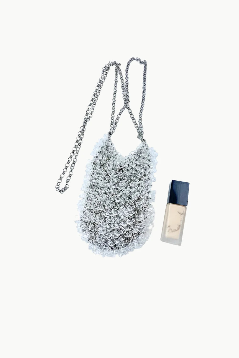 Small silver beaded crossbody bag with chain strap and liquid foundation nearby