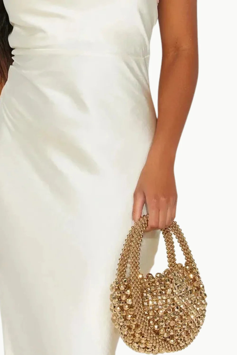 Woman in a cream slip dress holding a gold beaded handbag for stylish accessory shopping