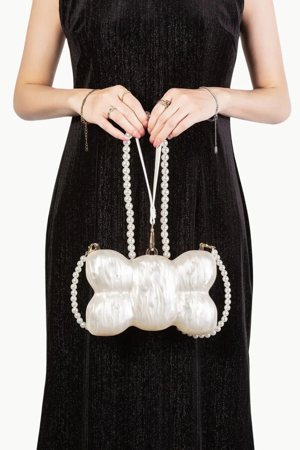 Woman in black dress holding a pearl mini bag with a bone-shaped pearl clutch