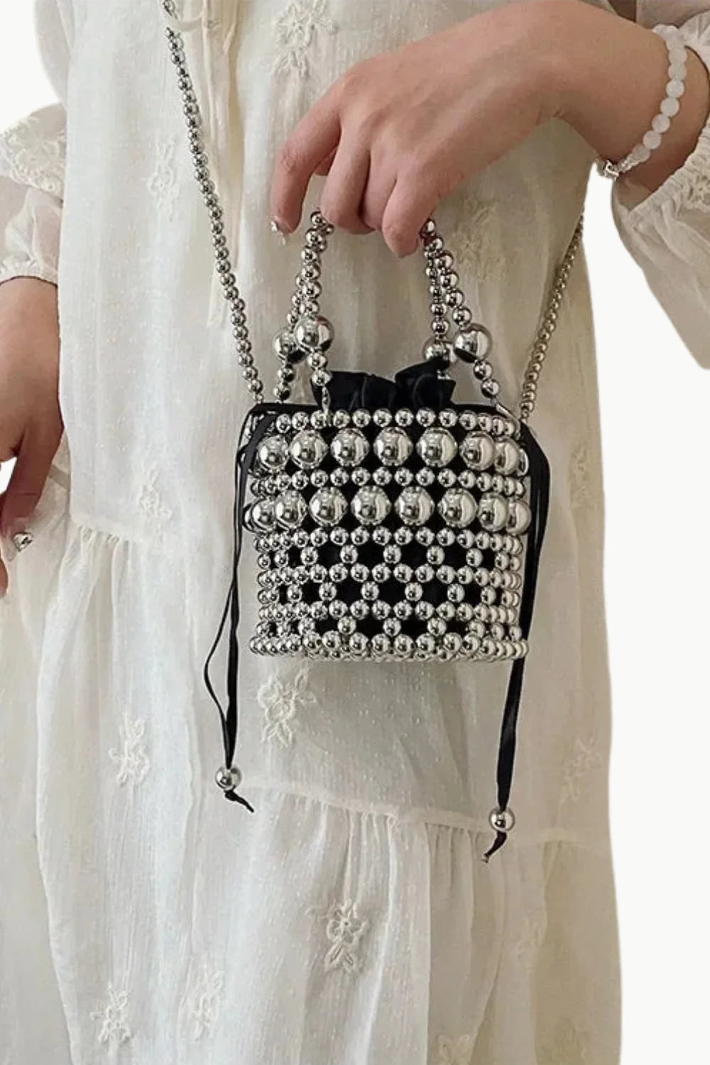 Silver bucket bag with beading, black drawstring closure, and beaded strap for stylish carry