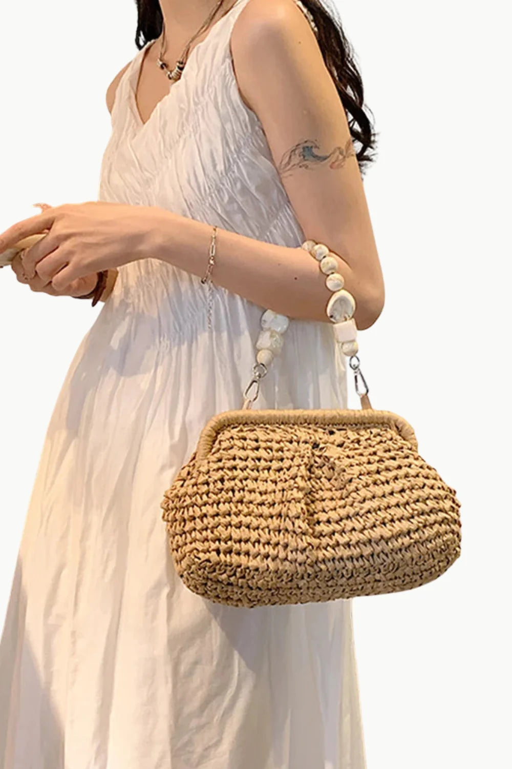Woman in white dress holding a woven straw beaded shoulder bag with a beaded handle